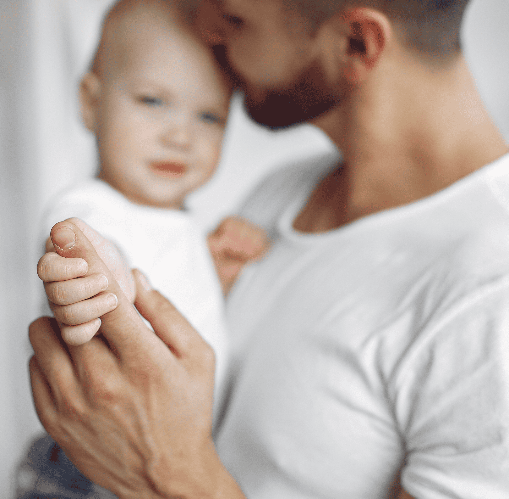 Father gently holding his baby's hand, kissing the baby's head